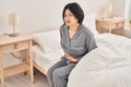 Young chinese woman suffering for menstrual pain sitting on bed at bedroom Royalty Free Stock Photo