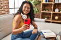 Young chinese woman using smartphone looking watch sitting on sofa at home Royalty Free Stock Photo