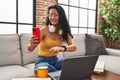 Young chinese woman using smartphone looking watch sitting on sofa at home Royalty Free Stock Photo