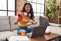 Young chinese woman using smartphone looking watch sitting on sofa at home Royalty Free Stock Photo