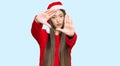 Young chinese woman wearing christmas hat doing frame using hands palms and fingers, camera perspective Royalty Free Stock Photo