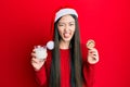 Young chinese woman wearing christmas hat holding cookies and milk sticking tongue out happy with funny expression Royalty Free Stock Photo