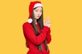 Young chinese woman wearing christmas hat holding symbolic gun with hand gesture, playing killing shooting weapons, angry face