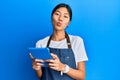 Young chinese woman wearing cook apron using touchpad looking at the camera blowing a kiss being lovely and sexy