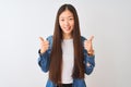 Young chinese woman wearing denim shirt standing over isolated white background success sign doing positive gesture with hand, Royalty Free Stock Photo
