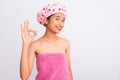 Young chinese woman wearing shower towel and cap bath over isolated white background smiling positive doing ok sign with hand and Royalty Free Stock Photo