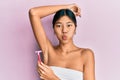 Young chinese woman wearing shower towel using razor puffing cheeks with funny face