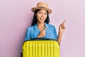 Young chinese woman wearing summer hat and holding cabin bag smiling and looking at the camera pointing with two hands and fingers Royalty Free Stock Photo
