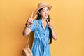 Young chinese woman wearing summer hat smiling looking to the camera showing fingers doing victory sign Royalty Free Stock Photo