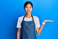 Young chinese woman wearing waiter apron smiling cheerful presenting and pointing with palm of hand looking at the camera Royalty Free Stock Photo