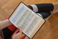 Young Christian woman holding open Holy Bible Book in her hands, top view