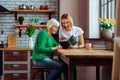 Young church volunteer reading Bible with pensioner at home kitchen