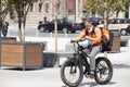 Young city delivery service courier riding an electric bike while looking at mobile phone