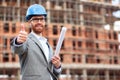 Young civil engineer or businessman standing in front of a construction site and showing thumbs up Royalty Free Stock Photo