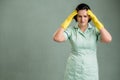 Young cleaning woman wearing a green shirt and yellow gloves has headache Royalty Free Stock Photo