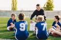 Young coach teaching kids on football field. Football coach coaching children