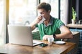 Young cold sick businessman in green t-shirt sitting at work, sneezing and cleaning his nose with tissue napkin