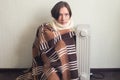 Young Cold Woman Wrapped In Blanket Sitting Near electric Heater At Home.
