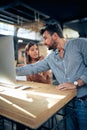 Young colleagues talking about business in the office. Man manager pointing to computer desktop screen, showing female worker Royalty Free Stock Photo