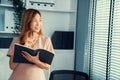 Young competent office lady, intern, secretary holding a log in office room.