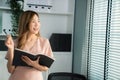 Young competent office lady, intern, secretary holding a log in office room.