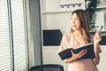 Young competent office lady, intern, secretary holding a log in office room.