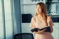 Young competent office lady, intern, secretary holding a log in office room.