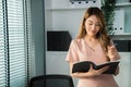 Young competent office lady, intern, secretary holding a log in office room.