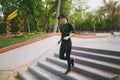 Young concentrated athletic beautiful girl in black uniform, cap with headphones doing sport exercises, warm-up before