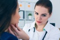 Young concentrated female doctor palpating lymph nodes of a patient. Doctor touching the throat of a patient.