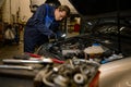 Young concentrated garage mechanic, technician, car engineer holding a flashlight lamp and repairing car under hood in the repair