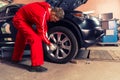 Young concentrated male auto mechanic standing near a black sedan and screwing car wheel Royalty Free Stock Photo