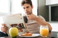 Young concentrated man reading newspaper while sitting in kitchen Royalty Free Stock Photo