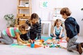 Young concentrated woman teacher sitting on floor with children, explaining how to draw with pencil in bright classroom. Royalty Free Stock Photo