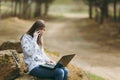 Young concerned business woman or student in casual clothes sitting on stone talking on mobile phone in city park or