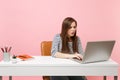 Young concerned woman have problem working on project while sitting at office with pc laptop isolated on pastel pink