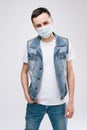 Young confidence man in medical mask and wearing denim clothes, standing over white isolated background. Royalty Free Stock Photo