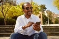 Young confident african man pointing hand on smartphone while sitting at sunny city park.Concept of happy business