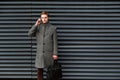 Young confident businessman in a gray coat and briefcase in his hand is talking on mobile phone against wall of modern Royalty Free Stock Photo
