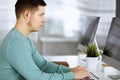 Young confident businessman, wearing a green pullover, is sitting at the desk in a modern office, while working on the Royalty Free Stock Photo