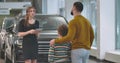 Young confident Caucasian woman explaining car specifications to male client. Back view of adult man choosing new