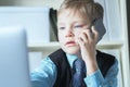 Young confident executive businessman boss boy in office talks on the phone sitting at the desk with laptop. Royalty Free Stock Photo