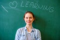 Young confident female high school student standing in front of chalkboard in classroom, looking at camera and smiling. Royalty Free Stock Photo