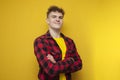 young confident guy in glasses with curly hair puts on a shirt on a yellow background