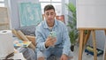 Young, confident hispanic man, a smiling art student, engrossed in a lively video call at his indoor studio