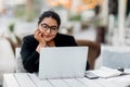 A young and confident Indian Asian woman smiles while sitting and working on her laptop in a stylish cafe on the street Royalty Free Stock Photo