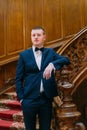 Young and confident newlywed groom posing in blue suit on old wooden stairs at vintage luxury hall Royalty Free Stock Photo