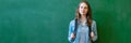 Young confident smiling female high school student standing in front of chalkboard in classroom, wearing a backpack.