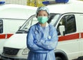 Young confident and successful Asian Korean medicine doctor woman in hospital scrubs and mask posing outdoors with ER ambulance