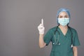 Young confident woman doctor in green scrubs is wearing surgical mask over grey background studio Royalty Free Stock Photo